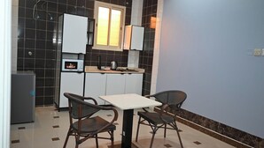 A compact kitchen with a microwave, kettle, and cabinets. There is a table with two chairs and a window above the sink. - Mawed Al Dyafa Serviced Apartments  (Riyadh)