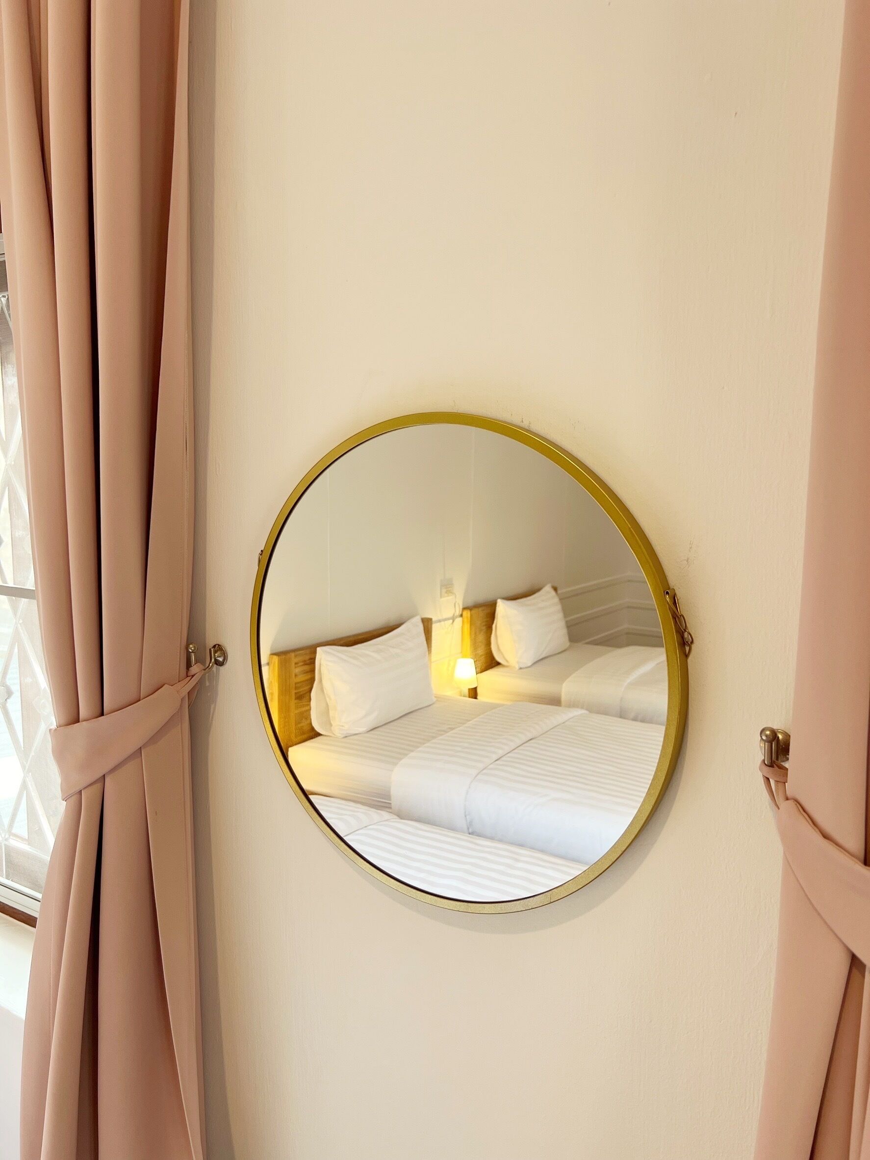 Una camera da letto con uno specchio rotondo a parete, un letto con biancheria bianca e tende ripiegate.