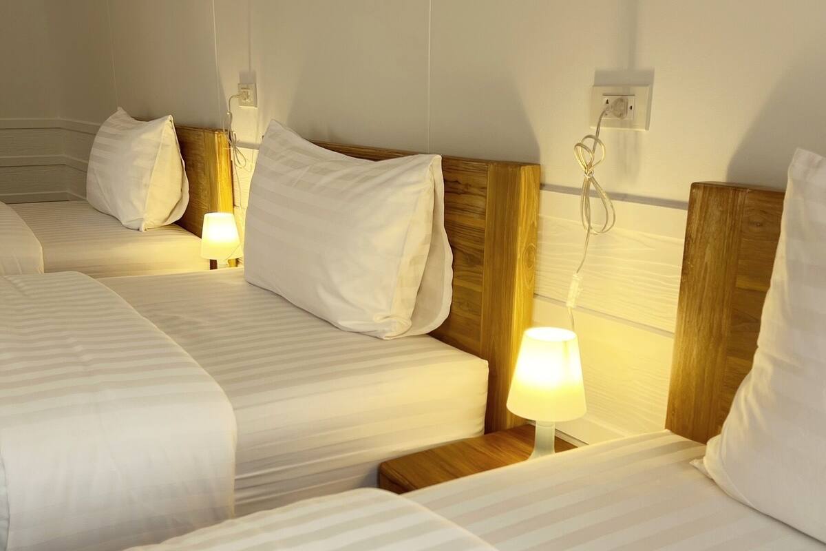 A hotel room with three beds, each with white bedding and wooden headboards. There are bedside lamps on each bed.