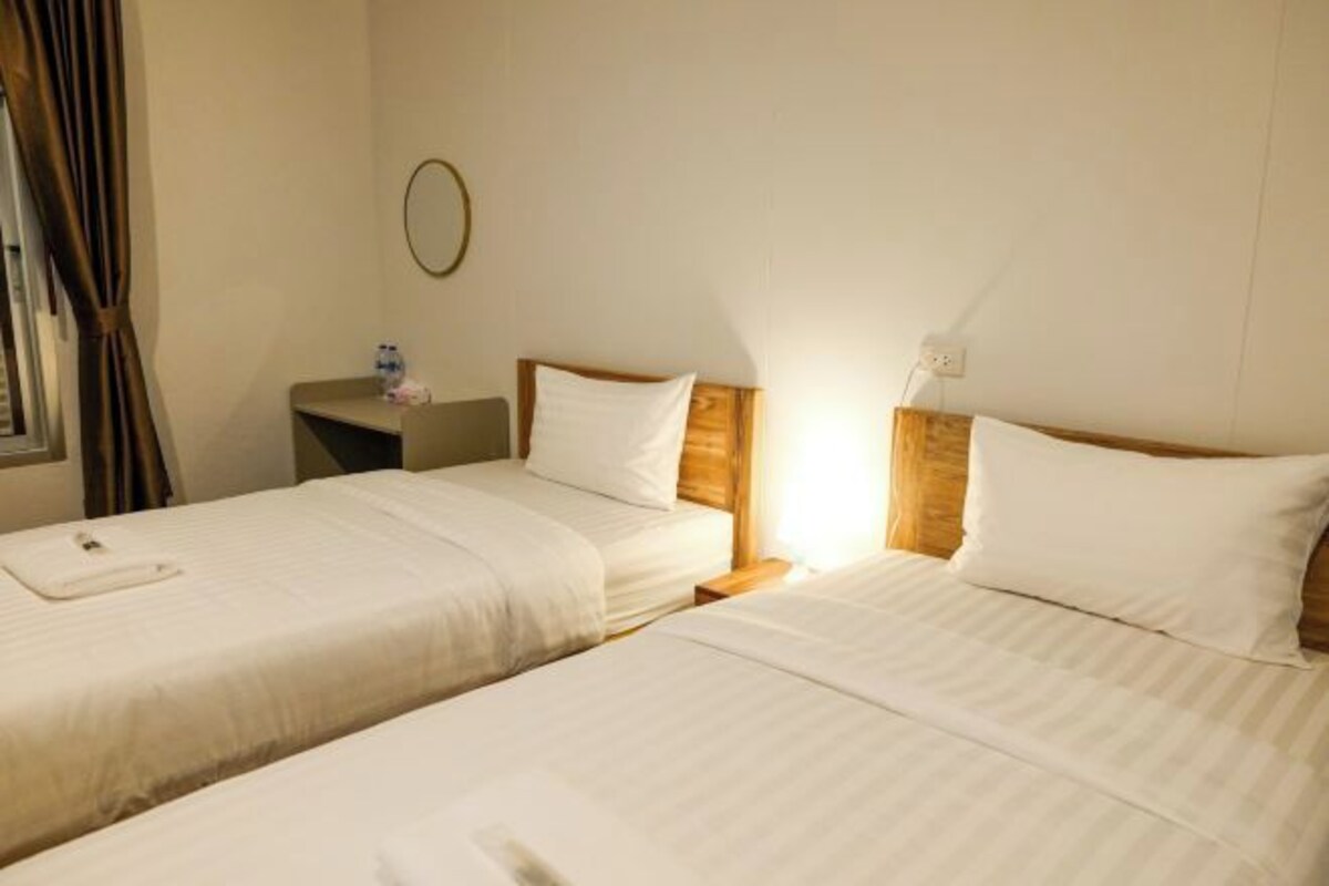 A hotel room with two beds, a bedside table with a lamp, and a window with curtains.