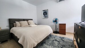 Quarto com cama, mesa de cabeceira, cômoda e um ventilador.
