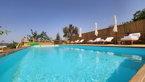 A clear blue swimming pool with wooden deck, white lounge chairs, and umbrellas.