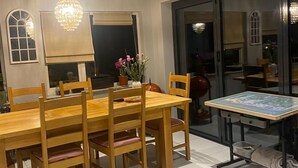 Un comedor con una mesa y sillas de madera, una araña y vistas a través de un ventanal.
