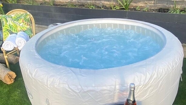 Una bañera de hidromasaje redonda con tapa blanca, una botella de champán y dos copas sobre una mesa redonda al lado.