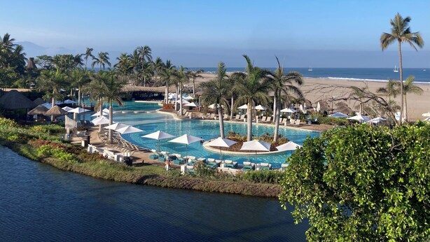A resort with a large pool, palm trees, and a beach view.
