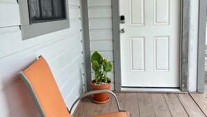 Een veranda met een witte deur, een bloempot en een oranje stoel.