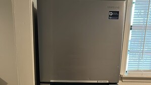 Een roestvrijstalen koelkast met een waterdispenser, in een keuken met betegelde vloer en een raam met zonwering.