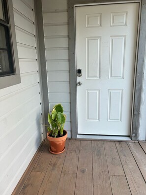 Une porte blanche avec un trou de serrure et une petite plante en pot sur un porche en bois.
