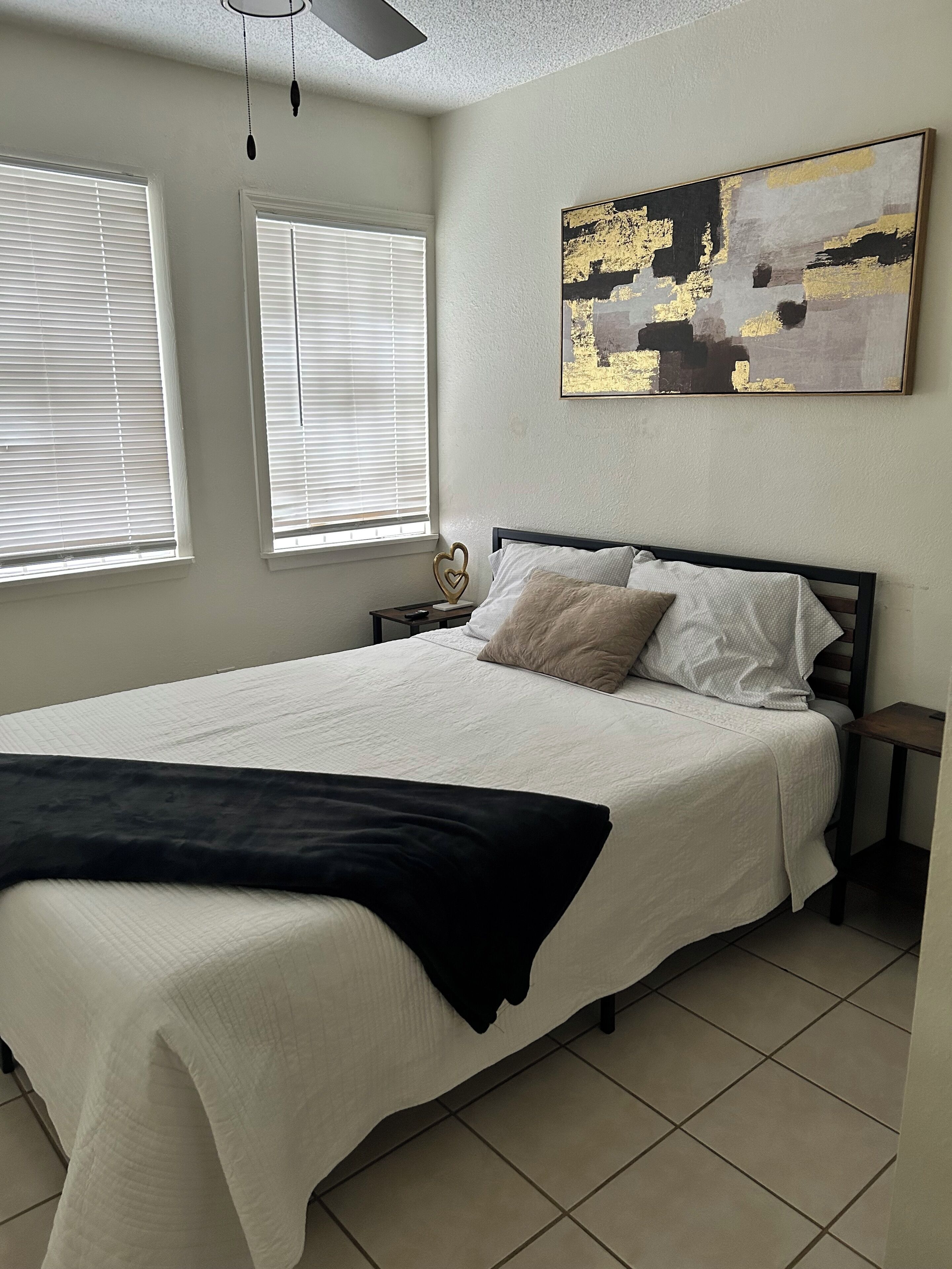 A bedroom with a bed, two bedside tables, a ceiling fan, and a window with blinds.