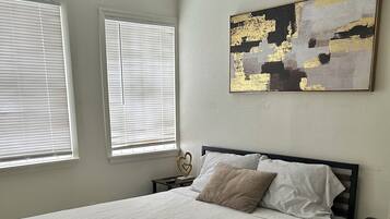 A bedroom with a bed, two bedside tables, a ceiling fan, and a window with blinds.
