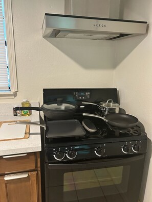 Una cocina con estufa, ollas y una ventana con persianas.