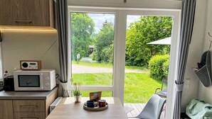 A compact kitchen with a microwave, a small table, and a chair. A window offers a view of a garden and a pathway. - Lovely apartment in villa for 4 people with WIFI, TV and pets allowed (Beilngries)