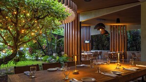 Un restaurante con una mesa de madera dispuesta para comer, rodeada de sillas y un árbol con luces.