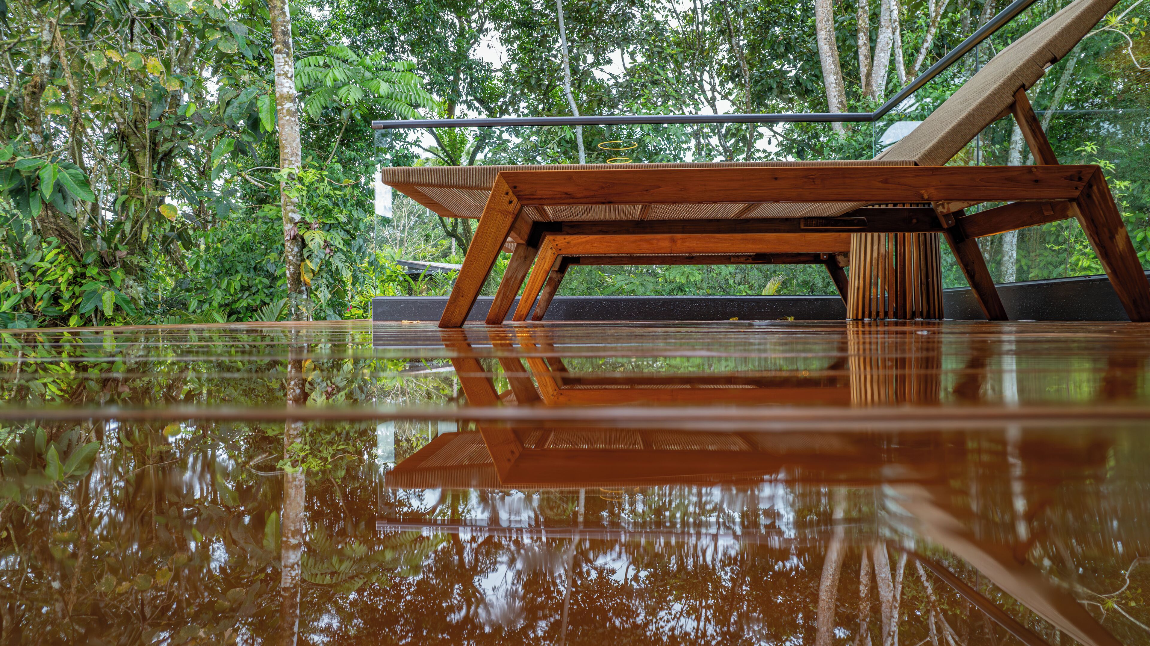 A wooden table with a glass top reflecting the surrounding greenery.