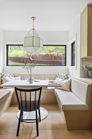 A modern kitchen with a built-in bench seating area, a dining table, and a large window offering a view of a garden. - Brand-New Vail 2BR Condo. Bright, Peaceful Retreat (Vail)