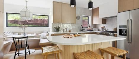 A modern kitchen with a large island, wooden bar stools, and a view of the outdoors.