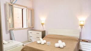 Hotellihuone, jossa on sänky, yöpöytä, yölamppu, lipasto, peili ja kaksi seinään kiinnitettyä valaisinta.