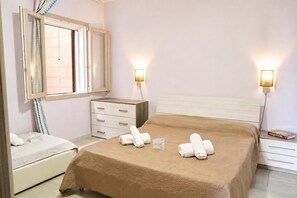 A hotel room with a bed, a bedside table, a nightstand, a dresser, a mirror, and two wall-mounted lights.