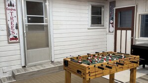 Una habitación con una mesa de fútbol de madera, paredes blancas y una puerta con un letrero que dice 'Christmas Trees'.