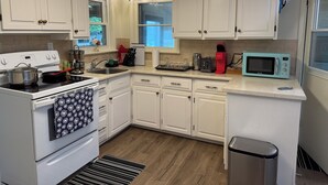 Una cocina con armarios blancos, estufa, microondas y fregadero.