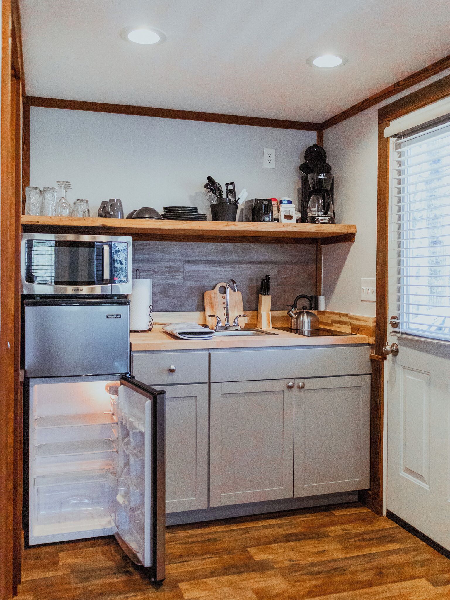 Cocina compacta con refrigerador, microondas, lavamanos y encimera de madera.