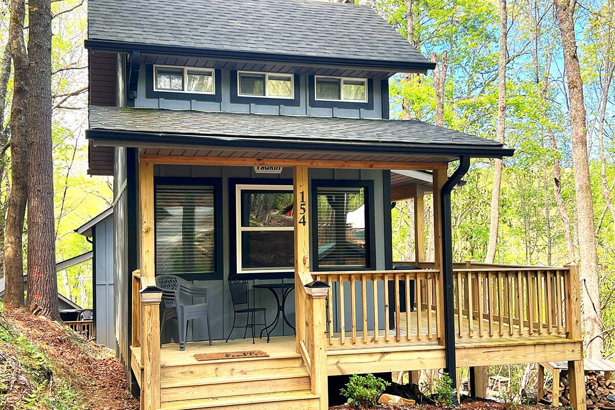 A two-story cabin with a wooden deck, a covered porch, and a small outdoor seating area.