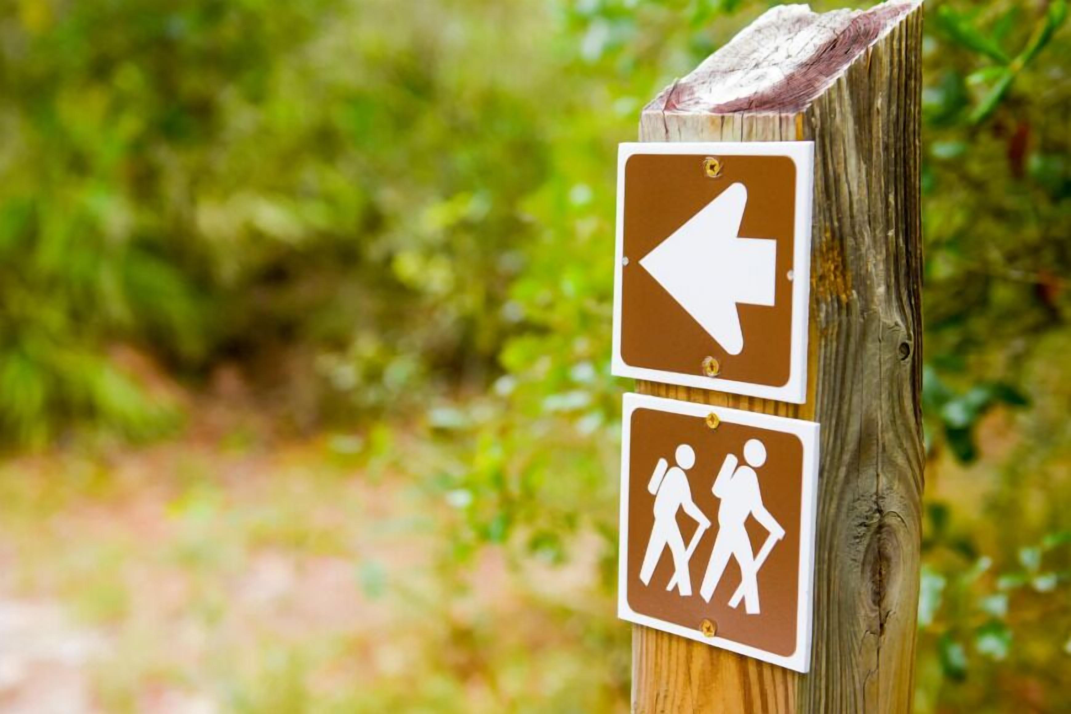 A wooden post with two directional signs, one pointing left and the other depicting a hiker.