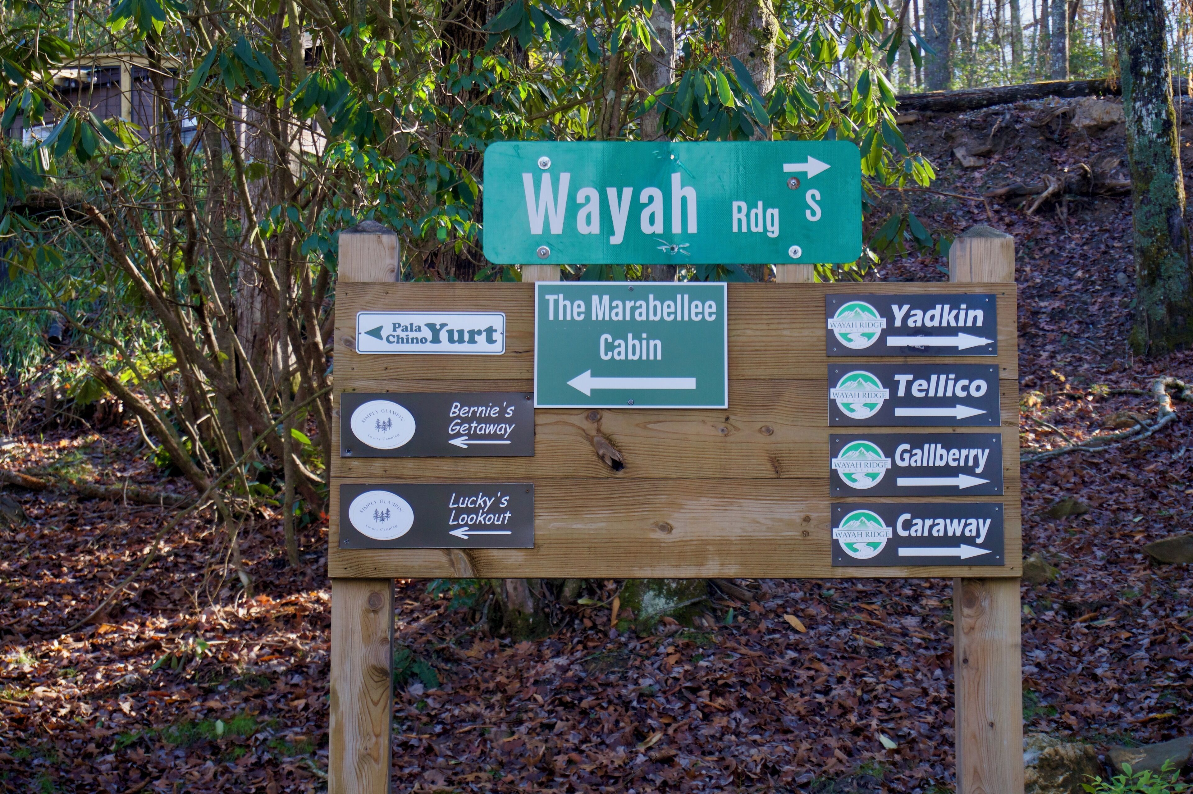 Een houten bord met richtingaanduidingen en pijlen naar verschillende bestemmingen, waaronder Wayah Rd, The Marabelle Cabin, Yadkin, Tellico, Gallberry en Caraway.