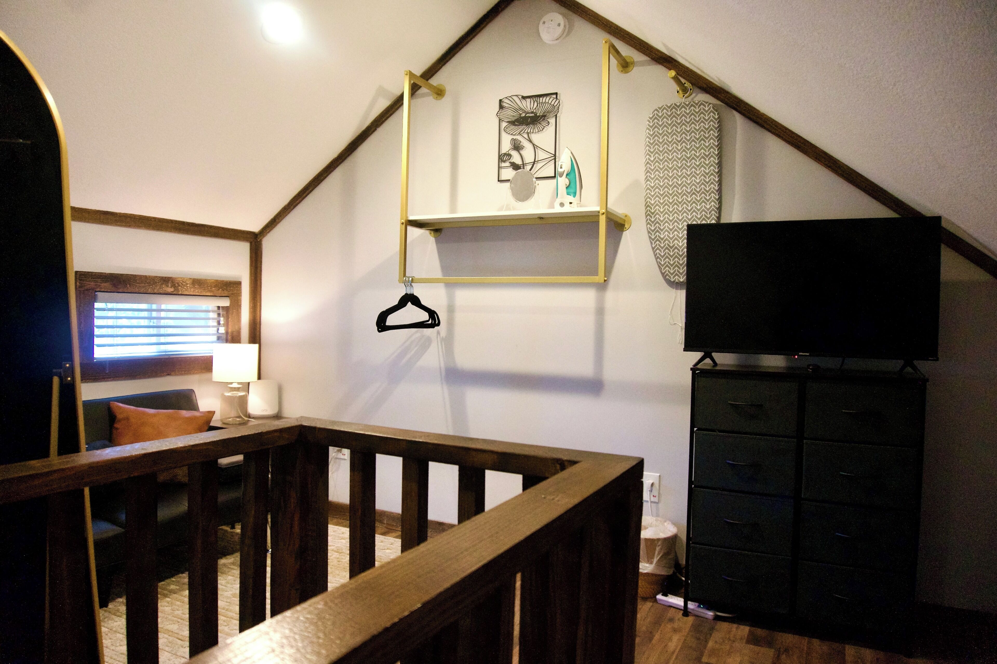 A room with a wooden staircase, a television on a stand, a black cabinet, and a wall-mounted shelf with decorative items.