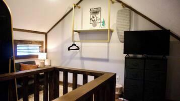 A room with a wooden staircase, a television on a stand, a black cabinet, and a wall-mounted shelf with decorative items.