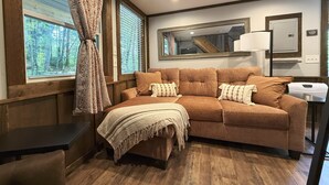 A cozy room with a brown sofa, a small table, and a window with blinds. - Wayah Ridge Escapes (Topton)