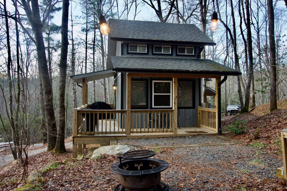 A cabin with a deck, a fire pit, and a car parked nearby.