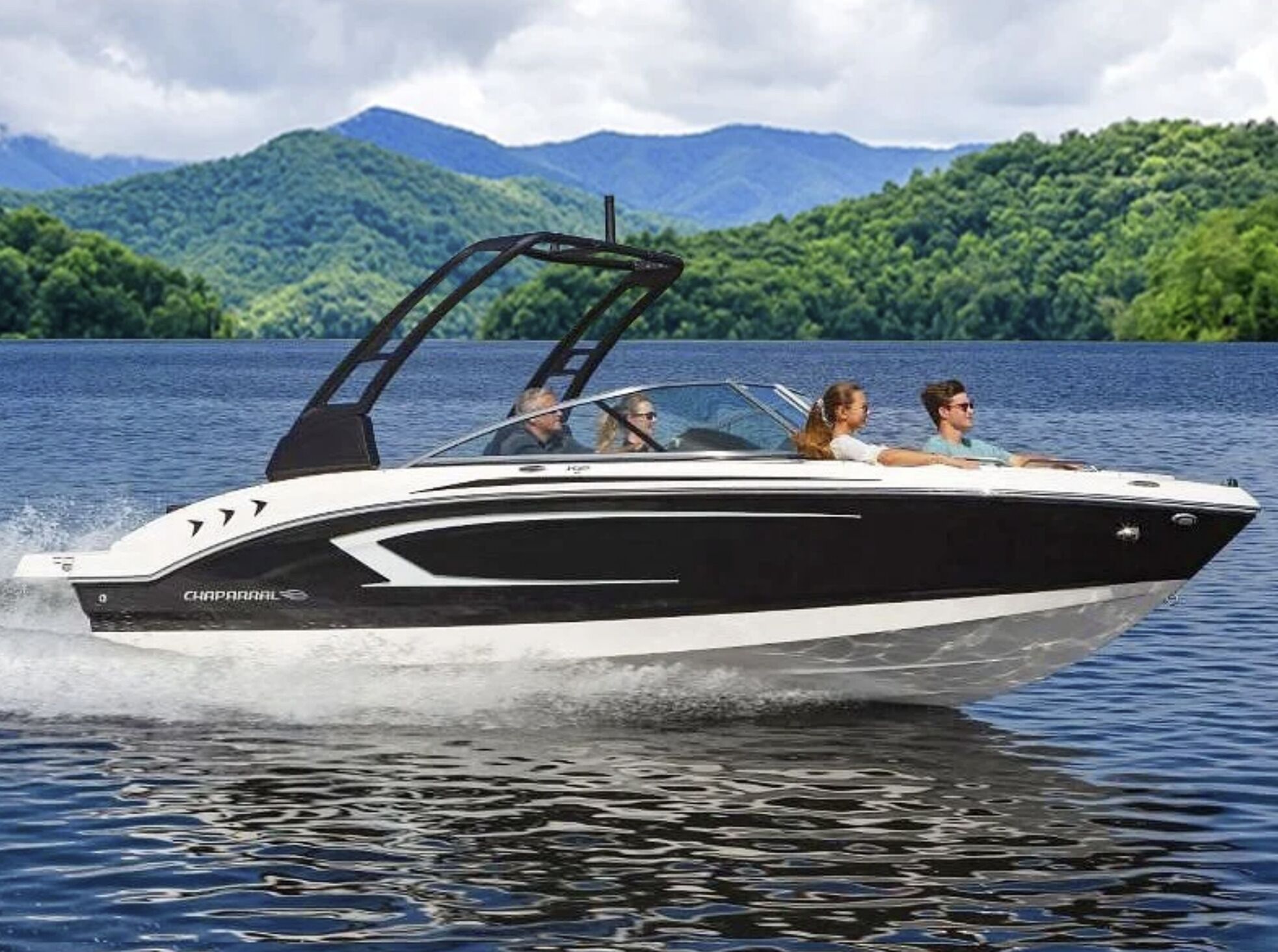 A speedboat with a cabin and a canopy, moving on a lake with mountains in the background.