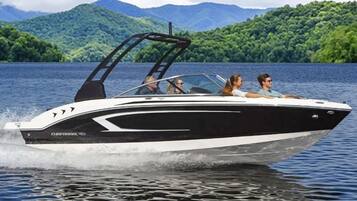 A speedboat with a cabin and a canopy, moving on a lake with mountains in the background.