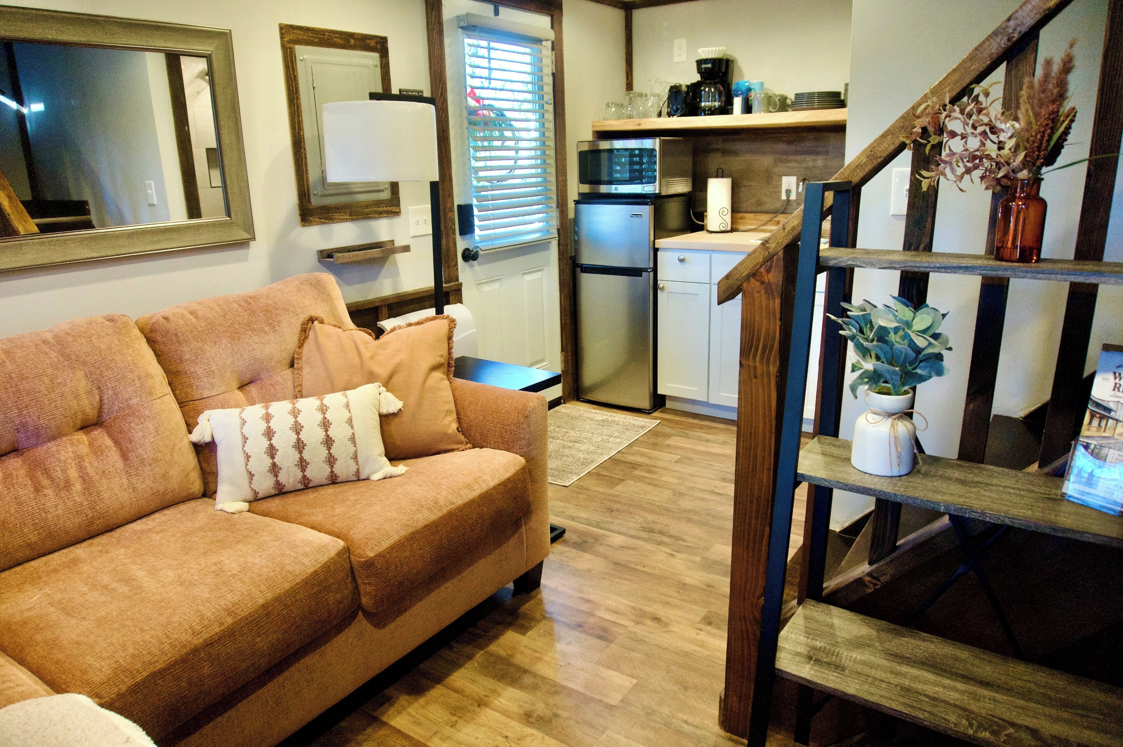 A cozy living room with a sofa, a small table, and a staircase leading to a kitchen area with a microwave and refrigerator.