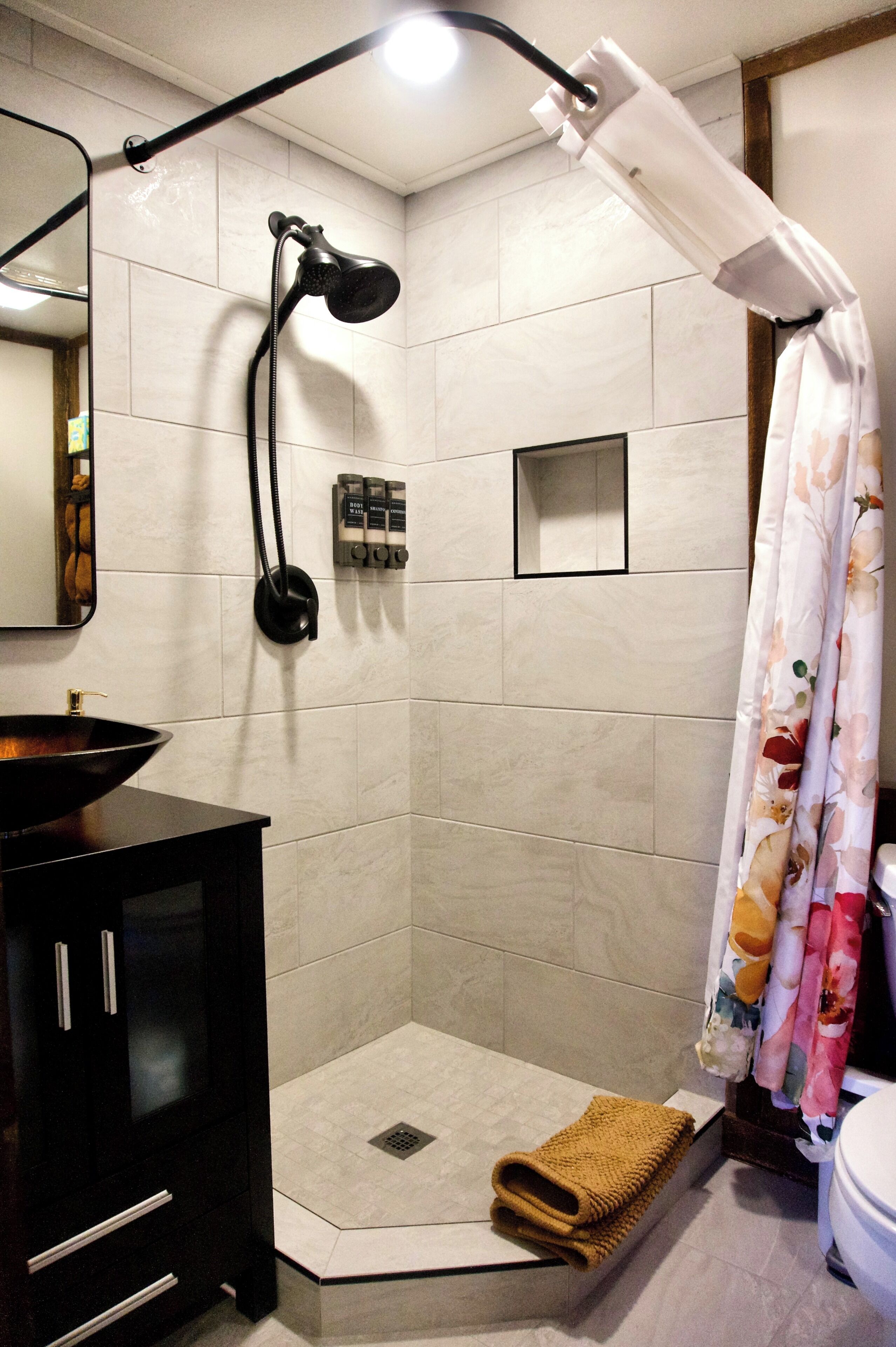 A corner shower with a handheld showerhead, a towel rack, and a toilet visible in the background.