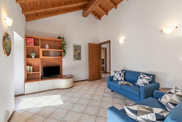 Una sala de estar con un sofá azul, una unidad de entretenimiento de madera y piso de baldosas.