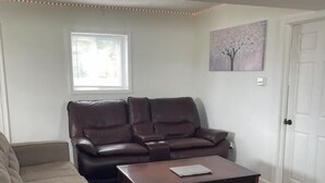 Una sala de estar con un sofá de cuero marrón, un sofá beige, una mesa de centro de madera y un tapete floral.