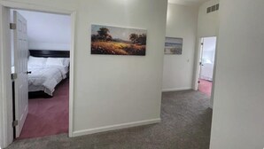 Un pasillo con una cama, un cuadro y una puerta que da a otra habitación.