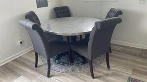 Una mesa de comedor redonda con cuatro sillas tapizadas, un alfombra estampado y un enchufe en la pared.