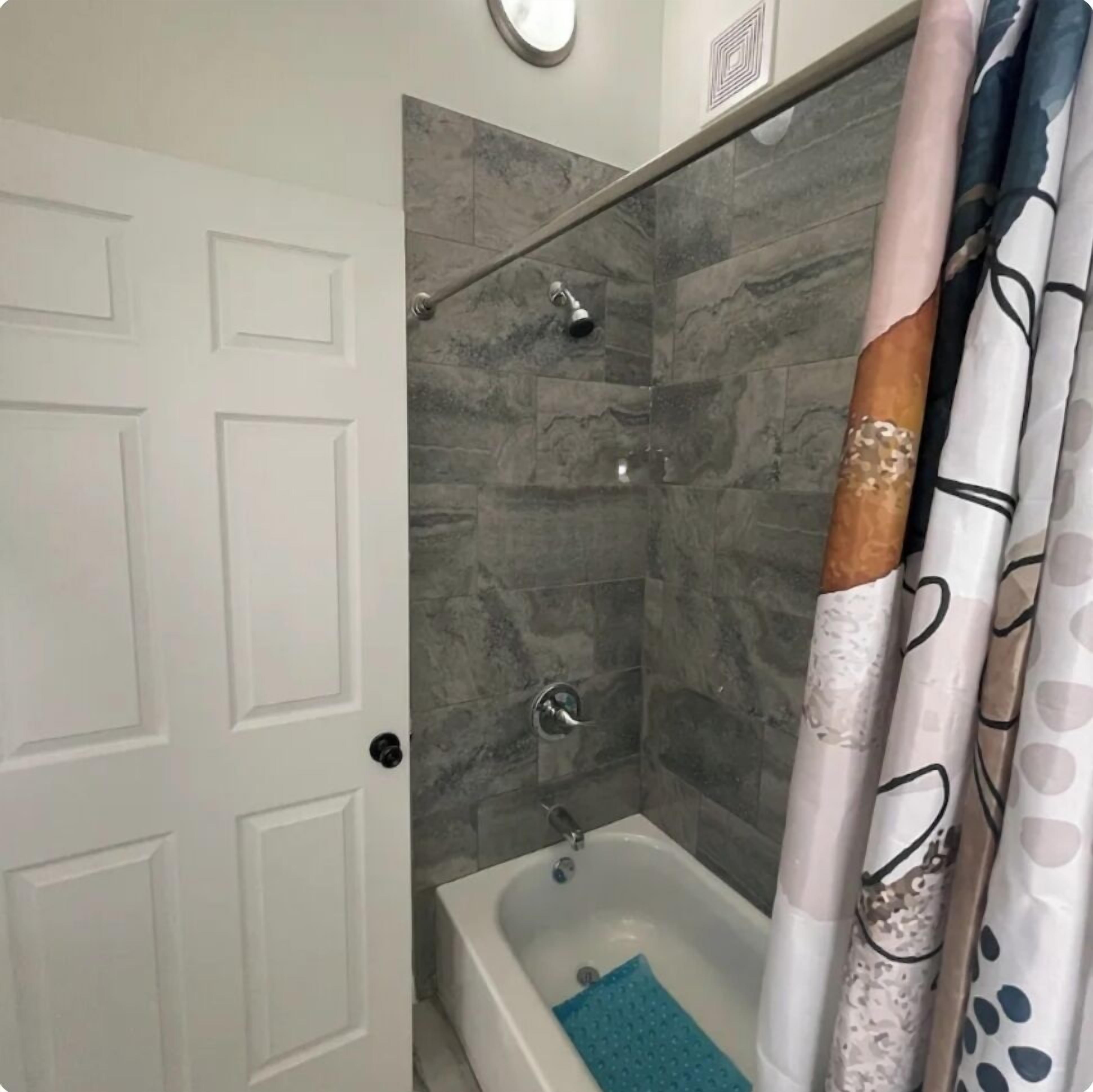A bathroom with a shower, a bathtub, and a white door.