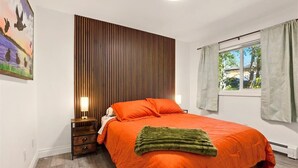 A bedroom with a large bed, a wooden slat headboard, a nightstand with a lamp, and a window with curtains.