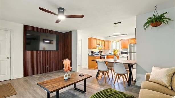 A modern living room with a wooden dining table, a sofa, and a kitchen in the background.