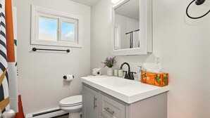 A bathroom with a white sink, a toilet, a window, and a mirror.