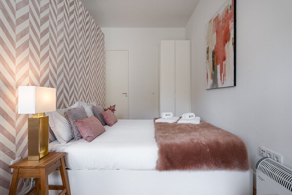 Una habitación de hotel con cama, mesita de noche, lámpara, una manta de piel sintética y un cuadro en la pared.