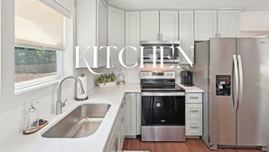 A modern kitchen with white cabinets, stainless steel appliances, a double sink, and a window with a roller blind. - Stylish 3BR Near Dining, Parks & Shops (Marietta)