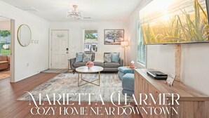 A cozy home with a living room, a dining area, and a kitchen. There is a chandelier, a painting, and a welcome sign. - Stylish 3BR Near Dining, Parks & Shops (Marietta)