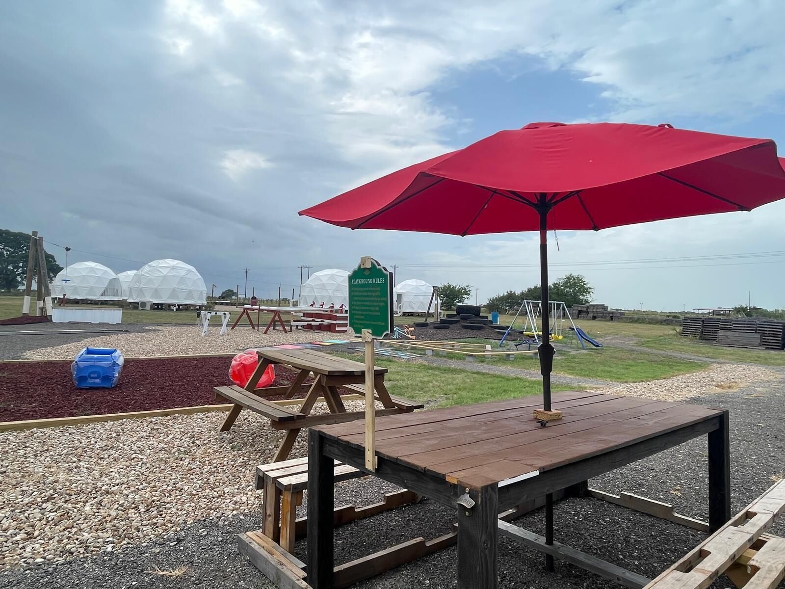 A playground with a red umbrella, picnic tables, and play structures.