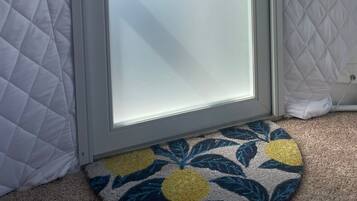 Une pièce avec une porte blanche matelassée, une porte en verre sur laquelle est apposée une pancarte indiquant « Veuillez préparer la chambre », et un tapis à motifs sur le sol.
