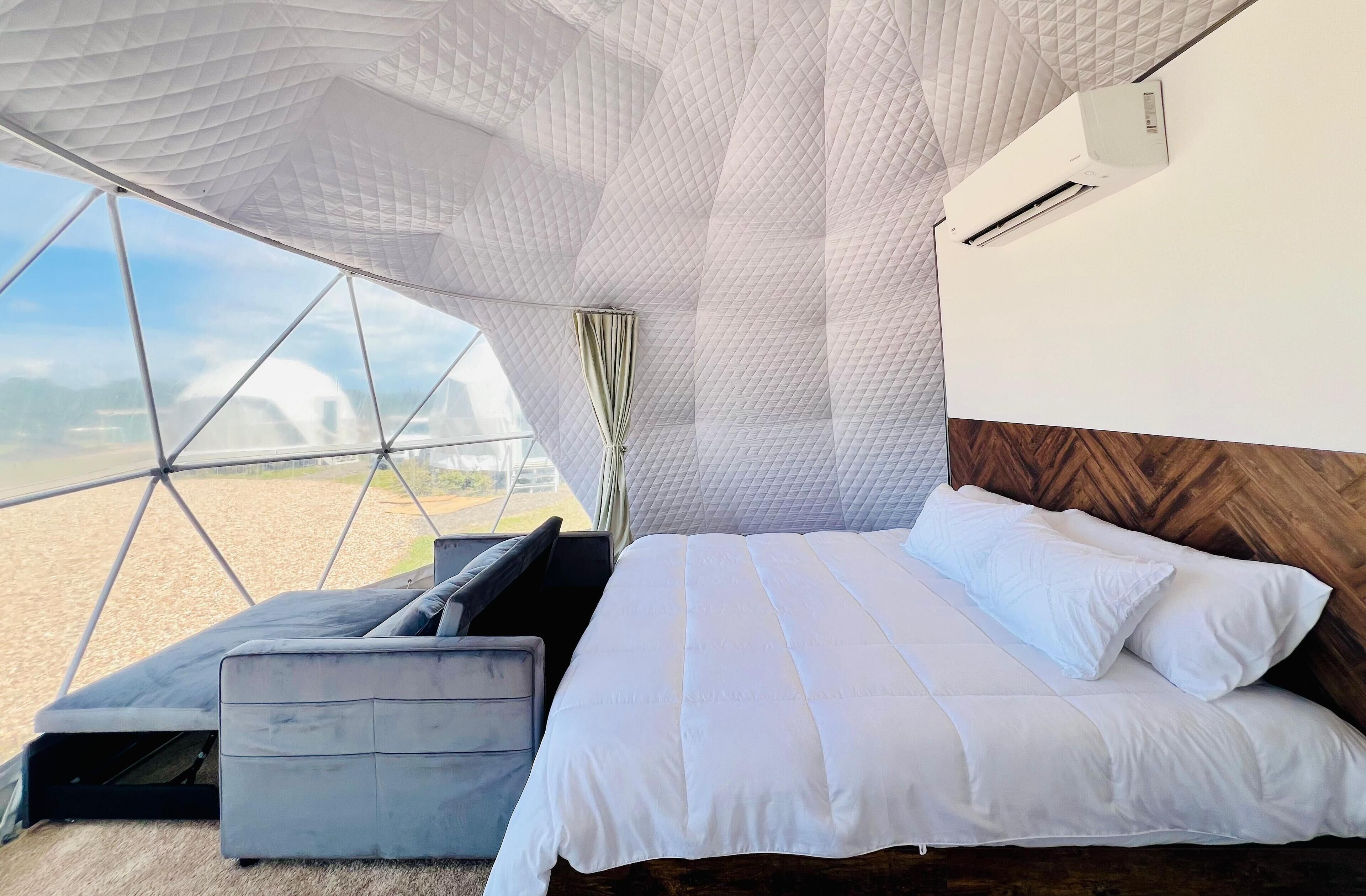 A modern room with a bed, a sofa, and a large window offering a view of the landscape.